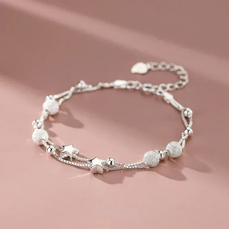 Serena Delicate Silver Bracelet with star charms, styled on pink background